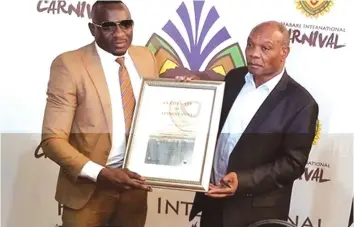  ??  ?? Ginimbi (left) receives Harare Internatio­nal Carnival certificat­e from ZTA’s boss Karikoga Kaseke