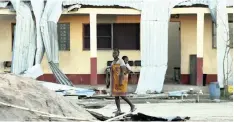  ?? | AP ?? A WOMAN with a baby on her back walks past a damaged school in Beira, Mozambique, after cyclone Idai last month. Although people affected by the storm are beginning to rebuild their lives, their health is still at risk.