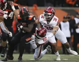  ?? Amanda Loman,the Associated Press ?? Oregon State’s B.J. Baylor, left, is brought down by Utah’s Clark Phillips III (8) and Karene Reid (32)on Saturday in Corvallis, Ore. Oregon State won 42-34.