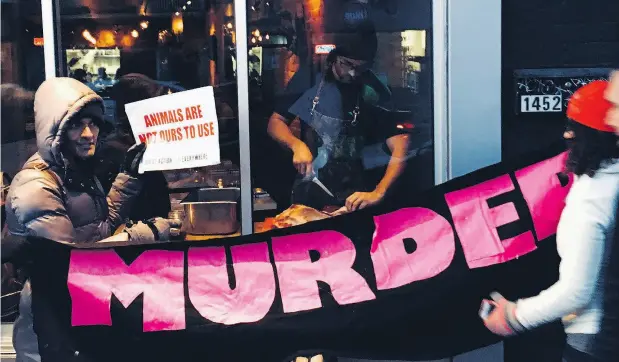  ?? MARNI JILL UGAR ?? As animal-rights protesters watch through the window, chef Michael Hunter carves a deer leg in his Toronto restaurant.