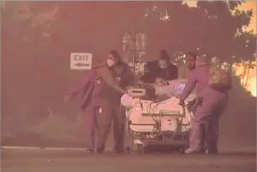  ?? Associated Press ?? IN AN IMAGE from video provided by KGO-TV/ABC7 News, hospital employees evacuate a patient from Kaiser Permanente Santa Rosa on Monday after a wildfire forced evacuation­s throughout the region.