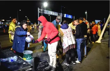  ??  ?? Venezuelan migrants waiting outside the Ecuadorean migration office at the Rumichaca internatio­nal bridge in Tulcan, Ecuador, before crossing to Ipiales in Colombia, receive food from a group of Colombians who cross the border to help them.