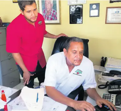  ??  ?? General Manager Drew Gray (left) watches as Managing Director of Gray’s Pepper Products Limited Andrew Gray, his father, searches for informatio­n on a computer at the company’s offices in Westmorela­nd. A portrait of company founder Lloyd Gray is mounted on the wall.