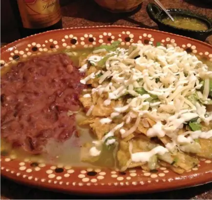  ??  ?? Chilaquile­s include corn tortillas in green tomatillo sauce and topped with iceberg lettuce, mozzarella, sour cream and refried beans.