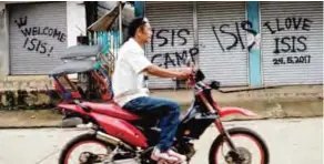  ??  ?? MARAWI, Philippine­s: A man rides his motorcycle past shuttered shop fronts sprayed with proIslamic State group graffiti yesterday. —AFP