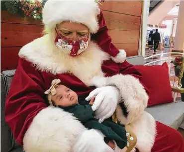  ?? Haven Daley / Associated Press ?? A Santa holds a baby at Stonestown Galleria in San Francisco. Amid a downturn in available Santas, about 15 percent fewer in one large database, some are busier than ever keeping up holiday spirits — with and without masks.