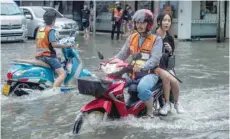  ?? — AFP ?? A passenger takes a ride on a motorcycle taxi on a flooded street in Bangkok on Saturday. Overnight torrential rains flooded many thoroughfa­res in Thailand’s capital city.