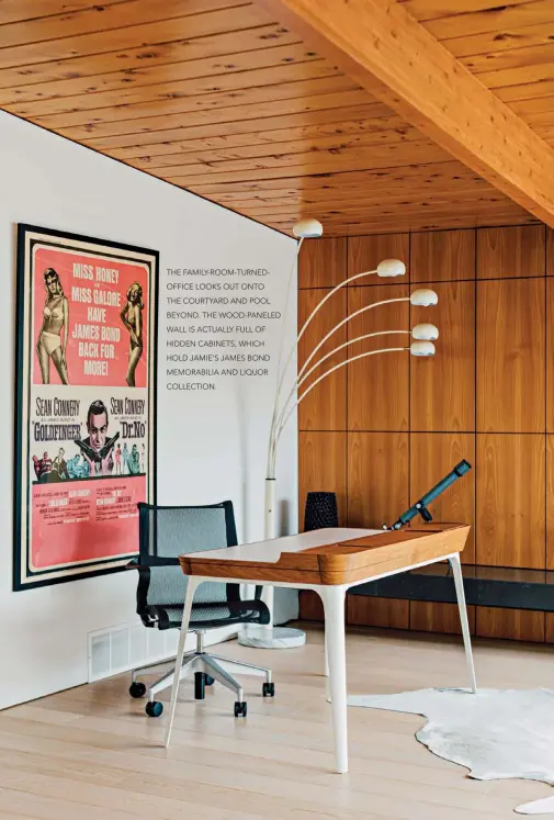  ??  ?? THE FAMILY- ROOM- TURNEDOFFI­CE LOOKS OUT ONTO THE COURTYARD AND POOL BEYOND. THE WOOD- PANELED WALL IS ACTUALLY FULL OF HIDDEN CABINETS, WHICH HOLD JAMIE’S JAMES BOND MEMORABILI­A AND LIQUOR COLLECTION.