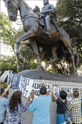  ?? RON BASELICE / THE DALLAS MORNING NEWS ?? Dallas activists tie pictures of abolitioni­sts to the statue of Robert E. Lee at Lee Park in Dallas on Tuesday. About 20 protesters gathered June 30 at the park to symbolical­ly “undedicate” the statue.