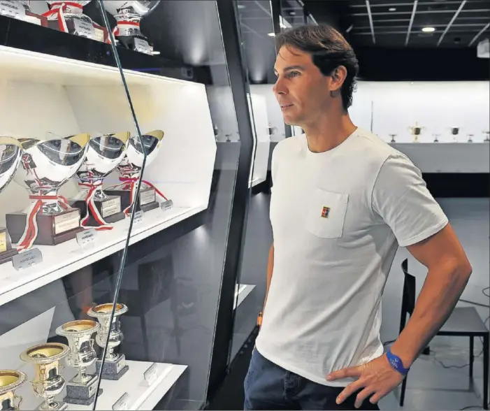  ??  ?? Nadal contempla algunos de los trofeos que tiene expuestos en el museo de su Academia en Manacor: en el estante de arriba, los de Montecarlo; en el de abajo, los de Roma.