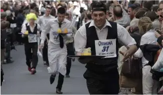  ?? ?? Des personnes habillées en serveurs portent des plateaux de boissons alors qu'elles participen­t à une course dans les rues de Paris.