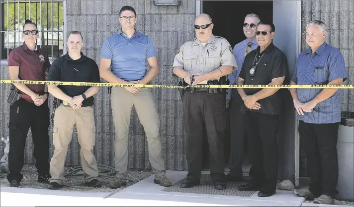  ?? ?? SURROUNDED BY LAW ENFORCEMEN­T PERSONNEL, Yuma County Sheriff’s Office Capt. James Amon (fourth from right) cuts, appropriat­ely enough, crime scene tape that served as the ribbon, to officially announce the operation of a new Rapid DNA Matching System in Yuma Wednesday morning.