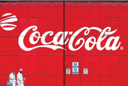  ?? REUTERS ?? Workers walk past a Coca Cola logo painted on a gate at a Coca Cola factory in Nairobi, Kenya.