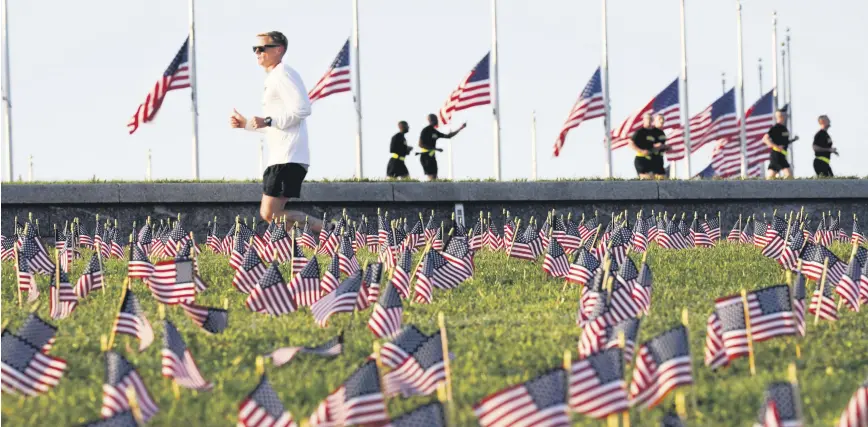  ??  ?? Morning joggers look over small flags that activists from the COVID-19 Memorial Project placed on the grounds of the National Mall to mark the 200,000 lives lost in the U.S. to COVID-19, in Washington, D.C., Sept. 22, 2020.