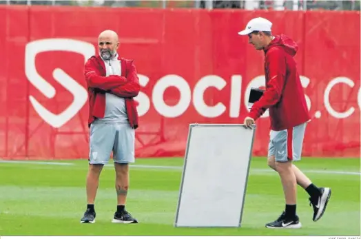  ?? JOSÉ ÁNGEL GARCÍA ?? Jorge Sampaoli permanece pensativo mientras un ayudante exhibe una pizarra de tácticas en el entrenamie­nto del Sevilla.