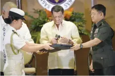  ?? — AFP ?? Philippine President Rodrigo Duterte (C) holds a .45 calibre handgun, one of 3,000 units handed over during a ceremonial turnover to the military, at Malacanang Palace in Manila on Tuesday, while military chief Eduardo Ano (R) looks on.