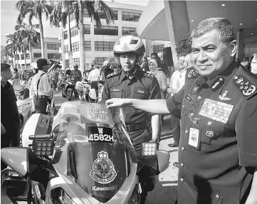  ??  ?? Khalid (right) putting a safety sticker onto a police motorcycle at the launch of Ops Selamat. — Bernama photo