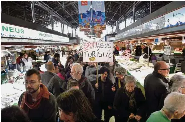  ?? — AFP ?? Tighter control: A protester holds a placard that reads: ‘Stop the tourist abuse’ in the La Boqueria market in Barcelona. Spanish cities are trying to contain a boom in Airbnb-type holiday rentals by allowing them only in ground-floor flats.