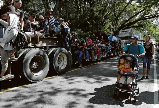  ??  ?? Homem com carrinho de bebê passa ao lado de caminhão de transporte de trator usado por imigrantes em Chiquimula, na Guatemala