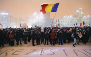  ?? VADIM GHIRDA, THE ASSOCIATED PRESS ?? A man waves the Romanian flag while standing with others next to the word "We resist" written in the snow during a protest outside government headquarte­rs, in Bucharest, Romania, Wednesday.