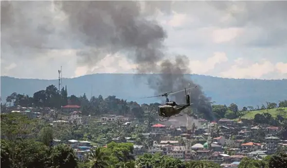  ?? AFP PIC ?? A helicopter flying through smoke billowing from houses after aerial bombings by Philippine Air Force planes on Islamist militant positions in Marawi, Mindanao, on Saturday. The Maute group’s strategy is similar to the Islamic State’s strategy in Mosul...