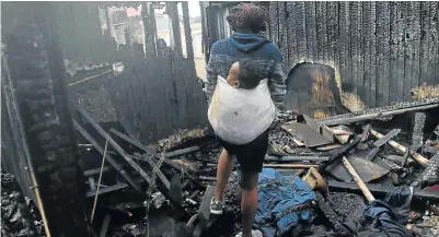  ?? Picture: MICHAEL PINYANA ?? A woman, with her child strapped to her back, goes through what remains following a fire that destroyed their home in Southernwo­od.