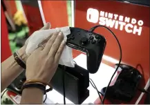  ?? STEVEN SENNE — THE ASSOCIATED PRESS FILE PHOTO ?? A game demonstrat­or cleans a game console at the Nintendo Switch exhibit at the Pax East conference in Boston last February. Launched in 2017, the Switch became a fast seller. In March 2020, it became hard to find a Switch as people searched for ways to be entertaine­d inside their homes.