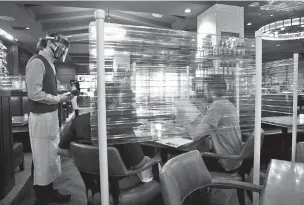  ?? JAE C. HONG/ASSOCIATED PRESS ?? Server Brandon Fricke, wearing a face shield and mask, takes orders recently from dine-in customers surrounded by protective dividers at Water Grill seafood restaurant in Los Angeles.