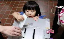  ??  ?? A girl casts her father’s ballot at a polling station in Tokyo