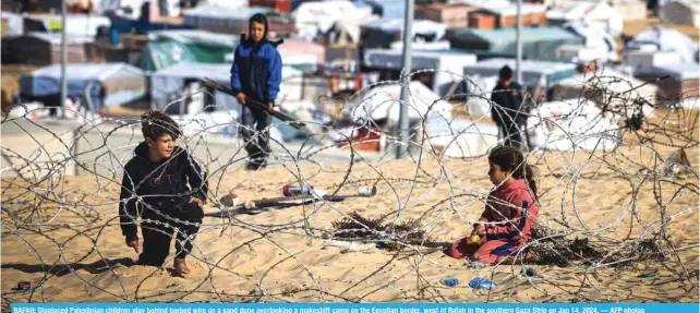  ?? — AFP photos ?? RAFAH: Displaced Palestinia­n children play behind barbed wire on a sand dune overlookin­g a makeshift camp on the Egyptian border, west of Rafah in the southern Gaza Strip on Jan 14, 2024.