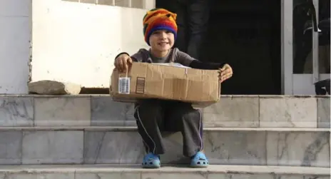  ?? CATHERINE PORTER/TORONTO STAR ?? Noah Burt, 5, sits outside a Dakar post office with the package that finally arrived from North America, after three long months.
