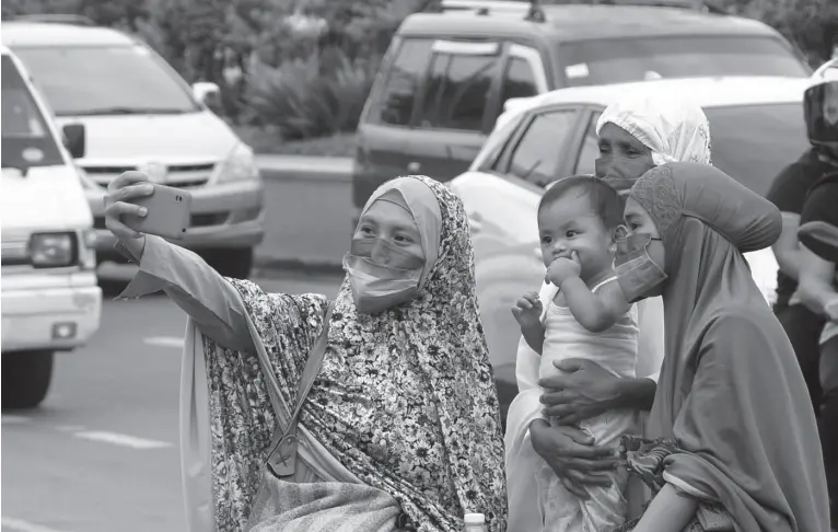 ?? ?? A WOMAN uses her mobile phone to take a family picture at the roadside along Quezon Boulevard after attending the prayers of Eid’l Fitr in the nearby mosque last May 2. BING GONZALES
