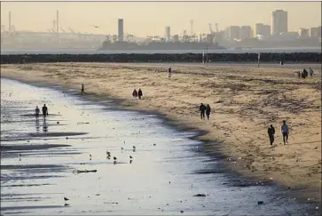  ?? Gary Coronado Los Angeles Times ?? PEOPLE STROLL the sands Tuesday in Seal Beach. The Orange County Health Care Agency announced this week that Seal and Sunset beaches have reopened. Beaches must be tested for two straight days to be cleared.