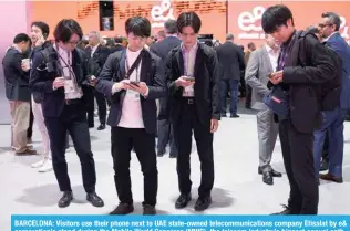  ?? ?? BARCELONA: Visitors use their phone next to UAE state-owned telecommun­ications company Etisalat by e& corporatio­n’s stand during the Mobile World Congress (MWC), the telecom industry’s biggest annual gathering, in Barcelona on Feb 27, 2024. — AFP photos