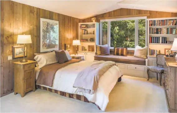  ??  ?? Wood-paneled walls, a sitting window and built-in bookshelve­s accent this bedroom in the redwood farmhouse.