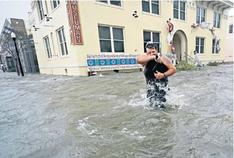  ??  ?? Trent Airhart wades through flood water whipped by high winds in Pensacola, Florida, where there were power cuts and extensive damage, including part of a bridge washed away