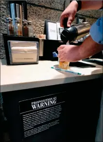  ?? ASSOCIATED PRESS ?? IN THIS SEPT. 2017 FILE PHOTO, a customer pours milk into coffee near a posted Propositio­n 65 warning sign at a Starbucks coffee shop in Los Angeles.