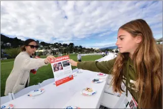  ?? SHERRY LAVARS — MARIN INDEPENDEN­T JOURNAL ?? Volunteers Ammie Bach of Greenbrae and her daughter Milla place a flyer with images of a kidnapped family at an empty Shabbat table with seating for 240at Dunphy Park in Sausalito. The number of seats represents the approximat­e number of hostages Hamas took in the surprise attack on Israel last month.