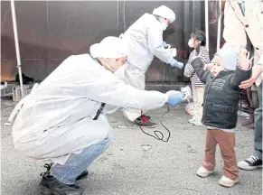  ?? REUTERS ?? Officials in protective gear check for signs of radiation in children near Japan’s Fukushima nuclear plant in March 2011.