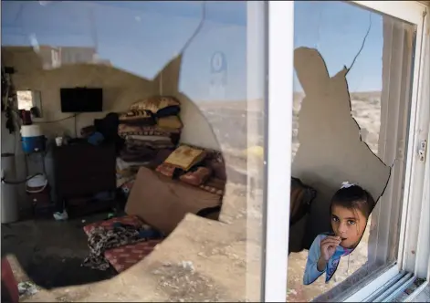  ?? (AP/Nasser Nasser) ?? A Palestinia­n girl is seen Sept. 30 through her family home’s shattered window following an attack by settlers from nearby settlement outposts on the Bedouin community in the West Bank village of al-Mufagara, near Hebron.