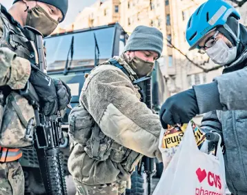  ??  ?? A National Guard soldier, left, stands outside the razor wire fencing that surrounds the US Capitol building. Right, a man distribute­s groceries to National Guard soldiers, on deployment since riots in the US capital