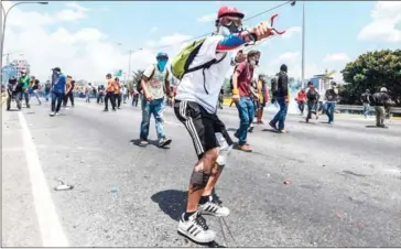  ?? JUAN BARRETO/AFP ?? An opposition activist aims a slingshot during a protest against President Nicolás Maduro in Caracas on Wednesday.