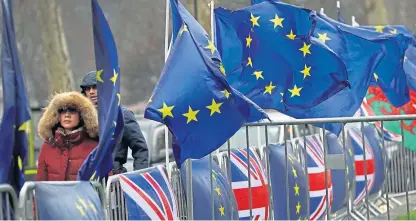  ?? AP. ?? People dressed for the cold weather pass by flags tied to railings outside parliament in London.