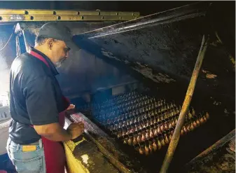  ?? J.C. Reid photos ?? George Gerard tends to sausage links in the smoker at Gerard’s Bar-B-Que.