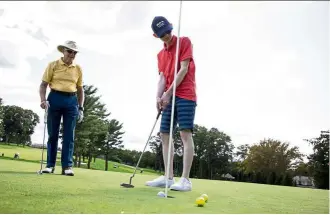  ??  ?? J.t. Stevens, who is visually impaired, putts the ball in the hole with the help of coach russo. Stevens has been playing golf since he was eight.