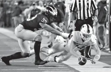  ?? Associated Press ?? Michigan State quarterbac­k Brian Lewerke (14) stretches for yardage as he is pushed out of bounds by Michigan linebacker Noah Furbush (59) during the first half of an NCAA college football game Saturday in Ann Arbor, Mich.