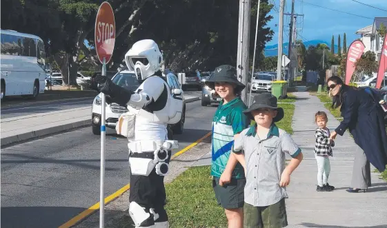  ??  ?? Helping hand ... Star Wars stormtroop­er Rob Wiseman helping children cross Fairways Dve at Clear Island Waters.