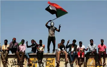  ??  ?? A Sudanese protester wearing a Guy Fawkes mask waves a national flag outside the defence ministry compound in Khartoum, Sudan. — Reuters photo