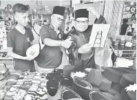  ??  ?? ADA GAYA:Yudha (kiri) melayani pelanggan yang mencuba songkok di gerainya. Sementara, Bolhassan Bakir (tengah) menunjukka­n tanda bagus kepada pilihan rakannya, Mohd Saleman Ibrahim.