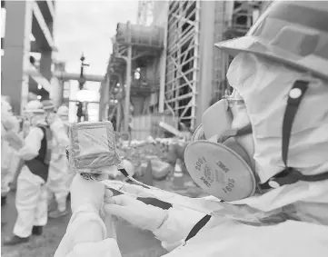  ?? — WP-Bloomberg photos ?? A worker measures the radiation in the air as employees in protective clothing prepare materials used to create a frozen undergroun­d wall to surround the crippled reactor buildings at Tokyo Electric Power Co.’s Fukushima Dai-ichi nuclear power plant in Okuma, Fukushima Prefecture, Japan, on July 9, 2014.